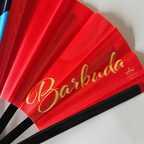 Close up of Antigua Barbuda flag inspired bamboo folding hand fan displaying the country's name in script font and displaying the Caribae Kiss logo.
