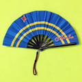 Flat lay of Aruba flag inspired bamboo folding hand fan along with black suede satchel bag with Caribae Kiss white logo print.
