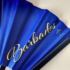 Close up of Barbados flag inspired bamboo folding hand fan displaying the country's name in script font and displaying the Caribae Kiss logo.