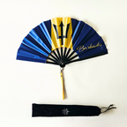 Flat lay of Barbados flag inspired bamboo folding hand fan along with black suede satchel bag with Caribae Kiss white logo print.