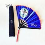 Belize flag inspired bamboo folding hand fan halfway open along with black suede satchel bag with Caribae Kiss white logo print.