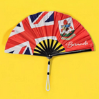 Flat lay of Bermuda flag inspired bamboo folding hand fan along with black suede satchel bag with Caribae Kiss white logo print.