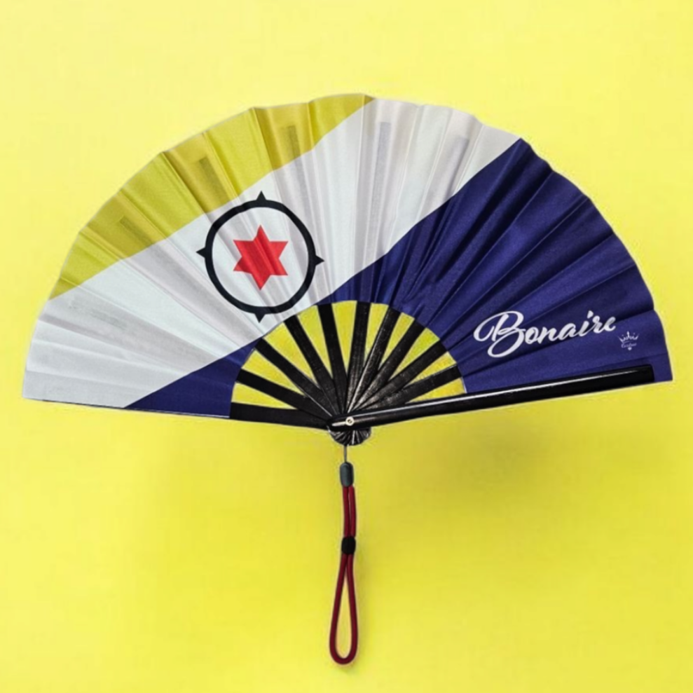 Flat lay of Bonaire flag inspired bamboo folding hand fan along with black suede satchel bag with Caribae Kiss white logo print.