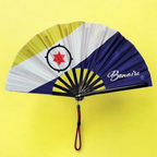 Flat lay of Bonaire flag inspired bamboo folding hand fan along with black suede satchel bag with Caribae Kiss white logo print.