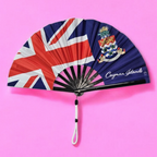 Flat lay of Cayman Islands flag inspired bamboo folding hand fan along with black suede satchel bag with Caribae Kiss white logo print.