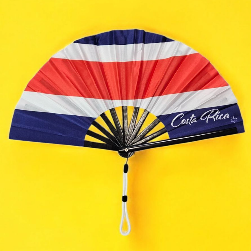 Flat lay of Costa Rica flag inspired bamboo folding hand fan along with black suede satchel bag with Caribae Kiss white logo print.d