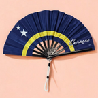 Flat lay of Curacao flag inspired bamboo folding hand fan along with black suede satchel bag with Caribae Kiss white logo print.
