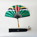 Flat lay of Dominica flag inspired bamboo folding hand fan along with black suede satchel bag with Caribae Kiss white logo print.