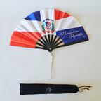 Flat lay of Dominican Republic flag inspired bamboo folding hand fan along with black suede satchel bag with Caribae Kiss white logo print.