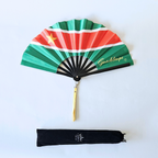 Flat lay of Guadeloupe flag inspired bamboo folding hand fan along with black suede satchel bag with Caribae Kiss white logo print.