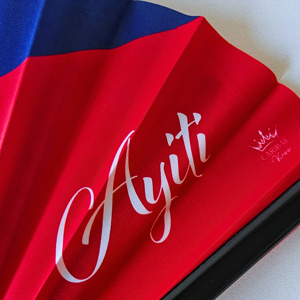 Close up of Haiti "Ayiti" flag inspired bamboo folding hand fan displaying the country's name in script font and displaying the Caribae Kiss logo.
