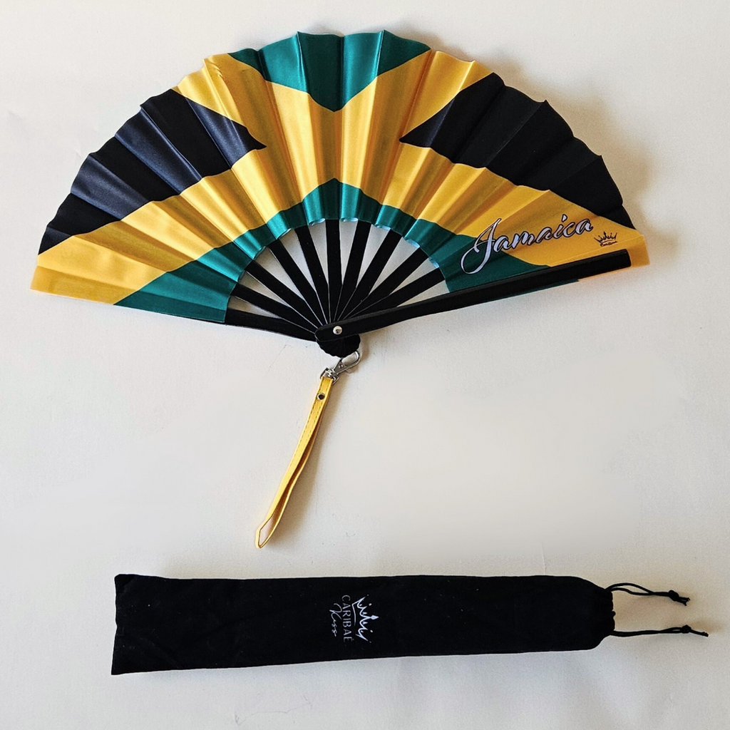 Flat lay of Jamaica flag inspired bamboo folding hand fan along with black suede satchel bag with Caribae Kiss white logo print.