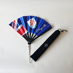 Anguilla flag inspired bamboo folding hand fan halfway open along with black suede satchel bag with Caribae Kiss white logo print.